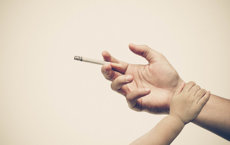 Stop smoking. Hand of a baby touching hand of a father with a cigarette. Dad stop smoking concept.の写真素材