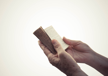 Old female hand holding an old small book of bibleの写真素材