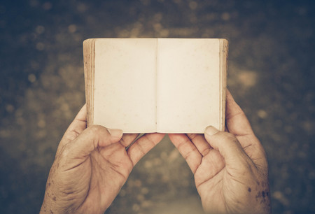 Old female hand holding an old small book with open blank pagesの写真素材