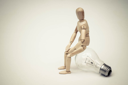 Wood Figure Mannequin sitting on an incandescent light bulb / Being stupid / Having no ideaの写真素材