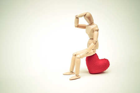Wood Figure Mannequin sitting sadly on a red heart waiting for loveの写真素材