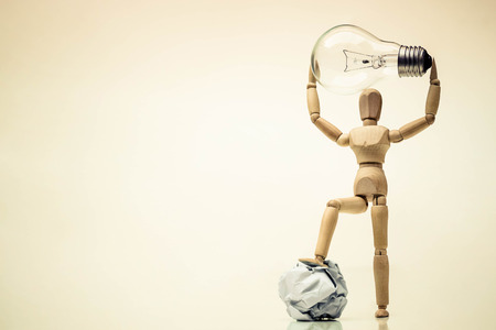 Wood figure mannequins carrying an incandescent light bulb and stepping on a crumpled paper ball / Change / Business with new idea and success conceptの写真素材