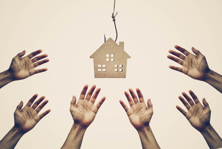 Hands reaching out for a house on a fish hook / Risks and negative sides of buying a house conceptの写真素材