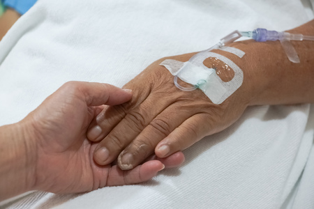 old hands holding each other with IV solution in a patient's hand