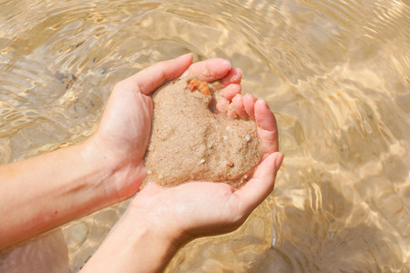 Female hands holding sand as a heart shape over a clear water / Love and protect nature concept