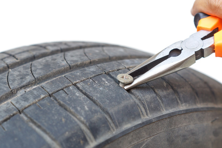 Removing a bolt from a flat tire using pliersの写真素材