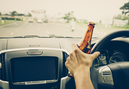 A driver holding alcoholic bottle while driving / Drunk driving conceptの写真素材