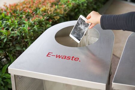 Hand dropping an old, damaged smartphone into a bin for e-waste garbageの写真素材