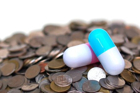 Two big capsule medicine on a pile of coins islated on white background / Increase drug cost conceptの写真素材