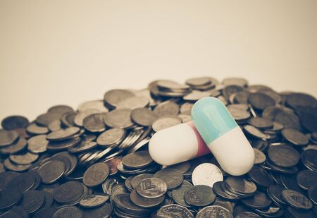 Two big capsule medicine on a pile of coins islated on white background / Increase drug cost conceptの写真素材