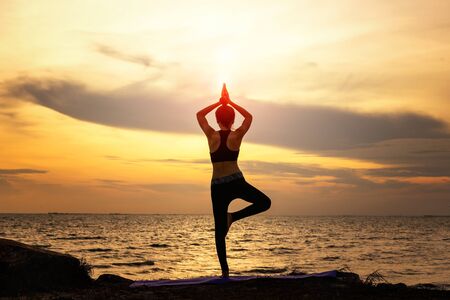 Silhouette young woman practicing yoga on the beachの写真素材