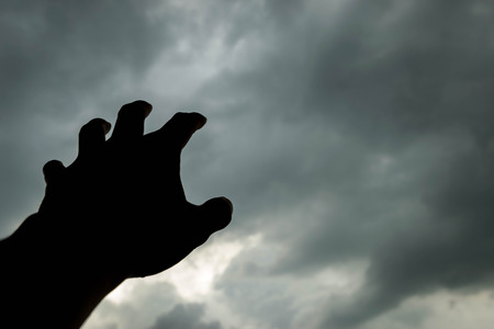 raising hand into the dark cloudy sky in silhouetteの写真素材