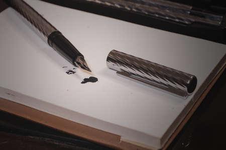 silver fountain pen vertical making a line and a splotch of ink on a white background