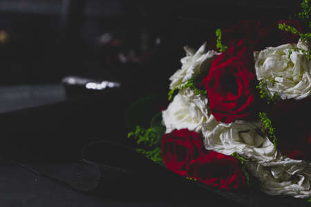 red and white flower bouquet placed on a wooden surface rolled in black sheet with a desaturated backgroundの写真素材