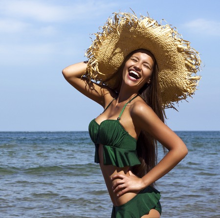 Woman in hat on beach. Beautiful smiling girl wearing green bikini poses near seaの写真素材