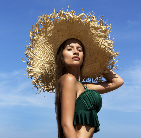 Woman in hat on beach. Beautiful gorgeous girl wearing green bikini poses near seaの写真素材