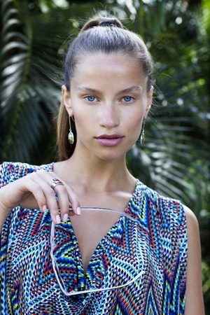 Portrait of beautiful fashion woman in tropics with black sunglasses. Sexy girl wearing color overalls, stylish earrings and ring posesの写真素材