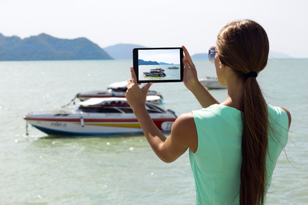 Woman traveler photographing sea view with digital tablet on pier of boat station. Phuket, Thailand