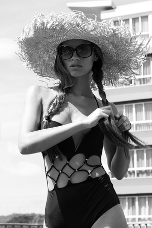 Woman in sunglasses and hat black stylish swimsuit with pigtails poses on roof enjoying landscape view. Phuket, Thailand. High fashion look.の写真素材