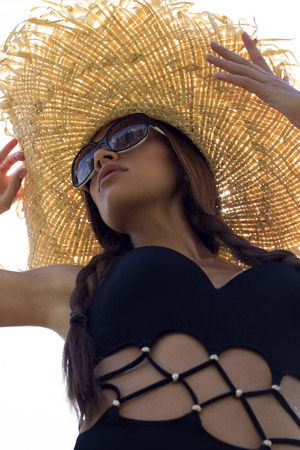 Woman in sunglasses and hat black stylish swimsuit with pigtails poses on roof enjoying landscape view. Phuket, Thailand. High fashion look.の写真素材