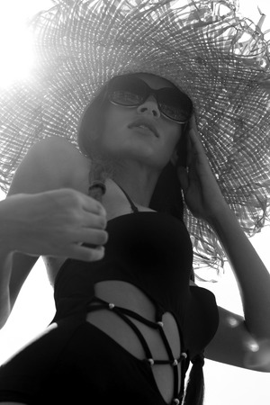 Woman in sunglasses and hat black stylish swimsuit with pigtails poses on roof enjoying landscape view. Phuket, Thailand. High fashion look.の写真素材