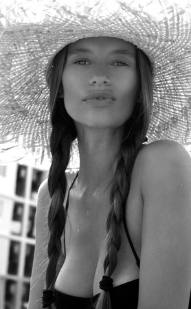 Woman in hat and black stylish swimsuit with pigtails poses on roof enjoying landscape view. Phuket, Thailand. High fashion look.の写真素材