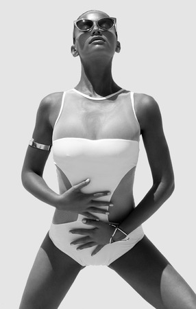 Woman in white swimsuit and golden sunglasses with hair up poses on isolated backgroundの写真素材