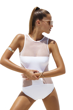 Woman in white swimsuit and golden sunglasses poses on isolated background. High fashion lookの写真素材
