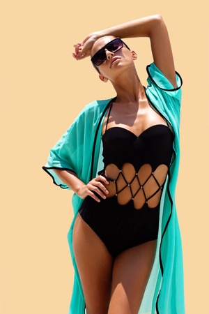Dancing woman in black swimsuit sunglasses and turquoise beach dress poses on color background. High fashion look.  Hair upの写真素材