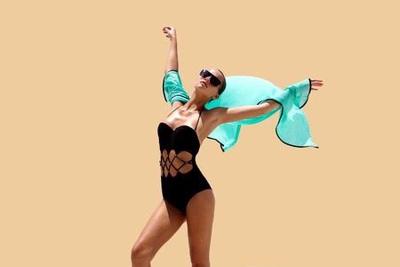 Dancing woman in black swimsuit sunglasses and turquoise beach dress poses on color background. High fashion look.  Hair upの写真素材