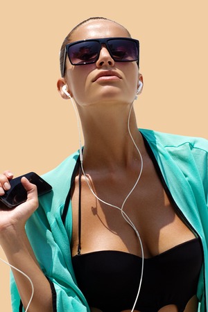 Dancing woman with headphones in black swimsuit and sunglasses poses on color background. High fashion look.の写真素材