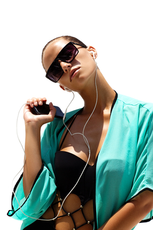 Dancing woman with headphones in black swimsuit and sunglasses poses on white isolated background. High fashion look.の写真素材
