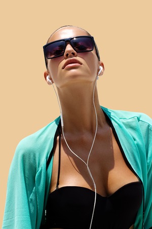 Dancing woman with headphones in black swimsuit and sunglasses poses on color background. High fashion look.の写真素材