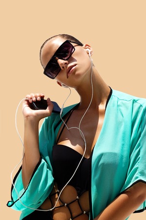 Dancing woman with headphones in black swimsuit and sunglasses poses on color background. High fashion look.の写真素材