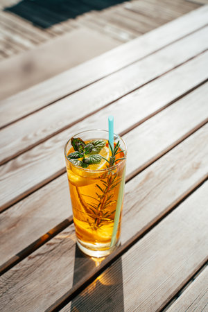 Enjoy a glass of homemade ice tea infused with fresh lemon and mint, beautifully presented on a wooden table under warm summer sunlight. Perfect for relaxation.の写真素材