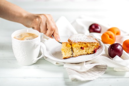 Homemade cake.Food preparation.fruit sweet cake with apricots and plums. Female hand breaking off a...