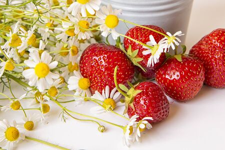 Scattered strawberries on a light background with a bouquet of chamomile flowers . Summer berry season.の写真素材