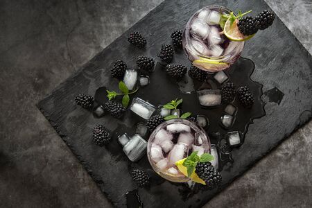 Seasonal soft drinks.Thirst in hot summer time. Two glasses of ice ,water ,lime and mulberry berries with mint on a dark background .Keto diet,soft drinks and alcoholic beverages. Fruit cocktailの写真素材