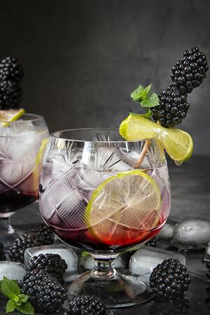 Seasonal soft drinks.Thirst in hot summer time. Two glasses of ice ,water ,lime and mulberry berries with mint on a dark background .Keto diet,soft drinks and alcoholic beverages. Fruit cocktailの写真素材