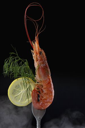 Red shrimp large close-up on a fork decorated with lemon and dill on a black background with steam. Marine food,background imageの写真素材