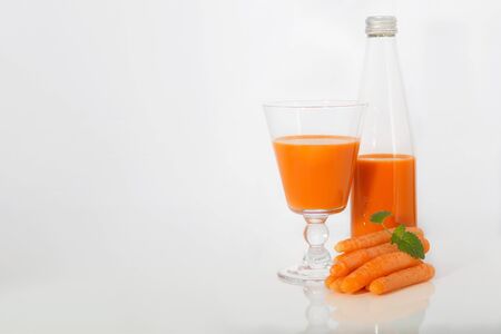 carrot juice in a glass and the bottle and lying next to a carrot with mint on white backgroundの写真素材
