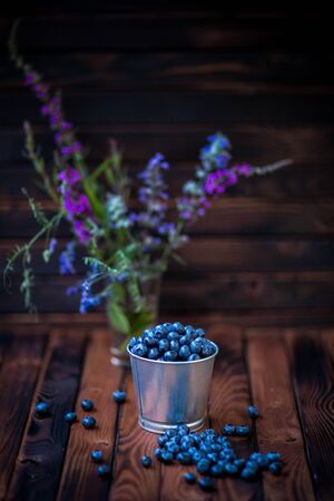 blueberries in a bucket on a dark wooden background .field flowers. rustic styleの写真素材