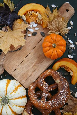 Autumn background.Chopping Board for kitchen made of wood on the table with leaves,pumpkin seeds , pretzels.の写真素材