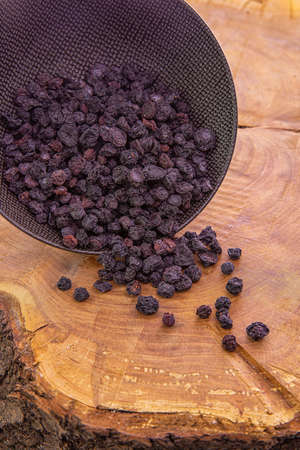 Dried blueberry berries are poured from a dark cup on a wooden backgroundの写真素材