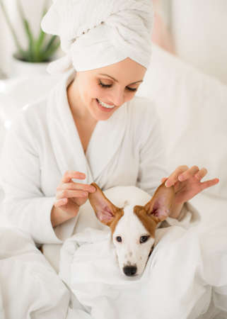 a girl in a white bath towel on her head and a bathrobe in the morning in bed with a dog opens a birthday gift. Loveの写真素材