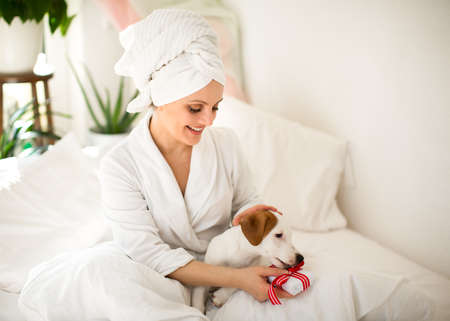 a girl in a white bath towel on her head and a bathrobe in the morning in bed with a dog opens a birthday gift. Loveの写真素材