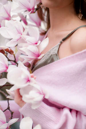 Body parts - female arms and shoulders.A woman in soft pink clothes holds blooming magnolia branches. Spring is April.の写真素材