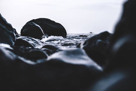 Small single boat in the distance and big rocks and water in the foreground