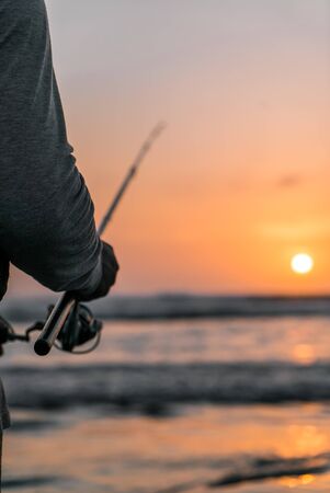 Man fishing on the beach at sunset