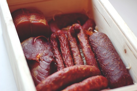 Assorted meat products including ham and sausages in a wooden box.の写真素材